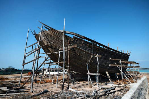 Construction of a wooden ship. Shipyard of traditional Dhow wooden boat on Iranian Qeshm Island. Tradition Lenj Fishing Boat in Qeshm Island in Southern Iran. Old wooden stealth smuggler's ship.