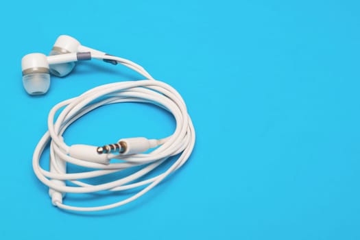 White headphones twisted on a blue background copy space