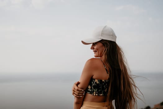 Woman travel sea. Happy tourist taking picture outdoors for memories. Woman traveler looks at the edge of the cliff on the sea bay of mountains, sharing travel adventure journey.