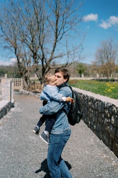 Dad hugs and kisses a little girl in his arms near a stone fence in the park. High quality photo