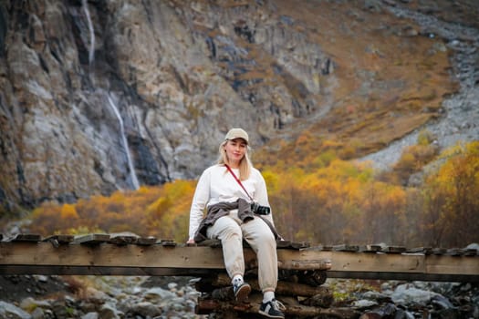 Domination of nature, girl sitting on the bridge, contemplating the power of the waterfall in the mountains