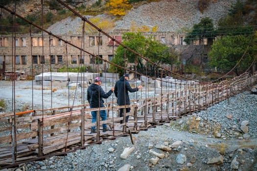 Two men bravely cross the river on a high suspension bridge
