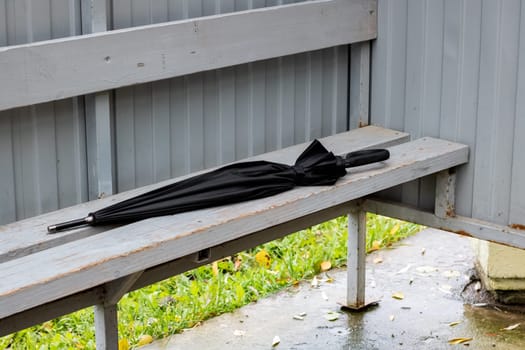 Black umbrella forgotten on a park bench close up