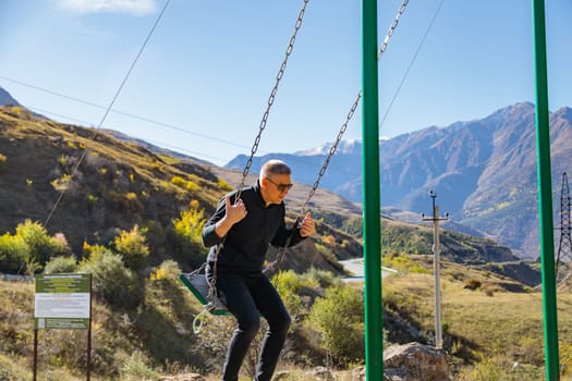 Man relaxing on a swing while enjoying the surrounding mountains and vast landscape.