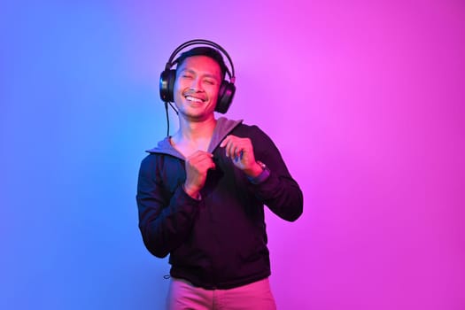 Attractive man enjoying favorite songs in headphones standing on red and blue neon light.