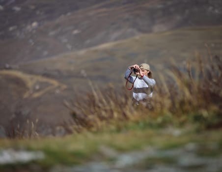 Young woman shooting delightful scenery uphill