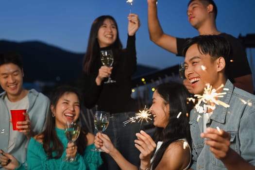 Group of young adult friends having fun a party on the rooftop with sparklers during sunset.