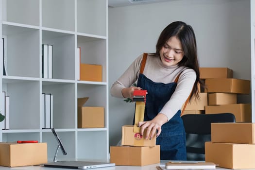 Young asian woman taping up a cardboard box in home office SME e-commerce business, relocation and new small business concept, SME concept.