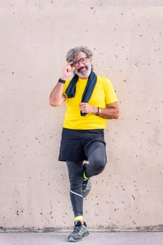 senior sports man with glasses smiling happy leaning on a wall looking at camera, concept of active and healthy lifestyle on the middle age, copy space for text