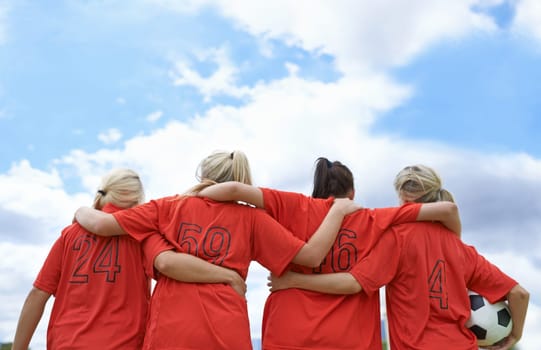 Woman, hug and back of soccer team ready for sports match, game or outdoor practice with blue sky. Rear view of female person or group of football players standing in unity with ball in nature.