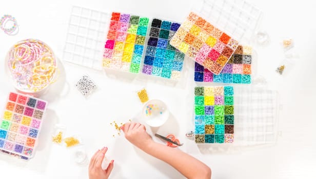 Flat lay. Little girl enjoys crafting colorful bracelets with vibrant clay beads set.