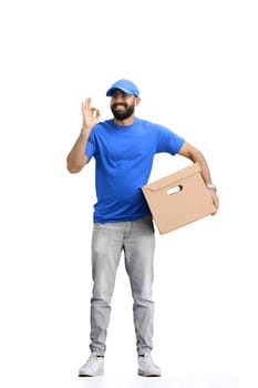 A male deliveryman, on a white background, in full height, with a box, shows the ok sign.