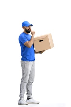 A male deliveryman, on a white background, in full height, with a box, shows a sign of silence.