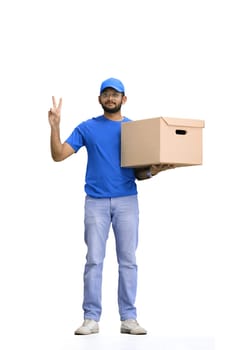 A male deliveryman, on a white background, in full height, with a box, shows a victory sign.