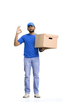 A male deliveryman, on a white background, in full height, with a box, shows the ok sign.
