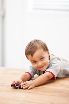 Cars, toys and portrait of child by table playing for learning, development and fun at modern home. Cute, sweet and boy kid enjoying a game with plastic vehicles by wood for childhood hobby at house