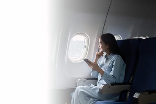 Asian people female person onboard, airplane window, using mobile while on the plane.