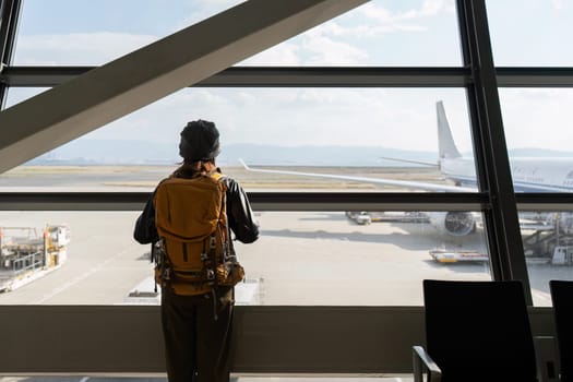 Traveler woman plan and backpack see airplane flight at the airport glass window.