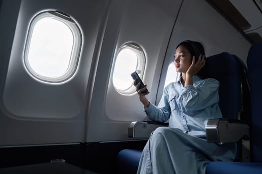 Asian people female person onboard, airplane window, using mobile while on the plane.