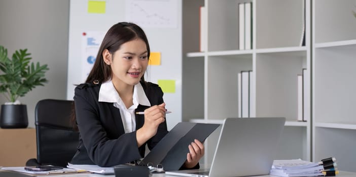 Portrait of young Asian woman working on laptop in modern office Perform accounting analysis, report investment data. Financial concepts and tax system.