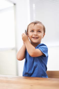 Toddler, boy and phonecall in house, happiness and communication with technology. Table, cheerful and conversation for learning, cellphone and excited for child development, mobile and digital.