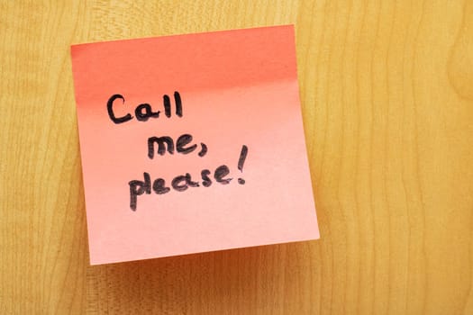 Pink paper sticker with the inscription Call me, please on wooden board