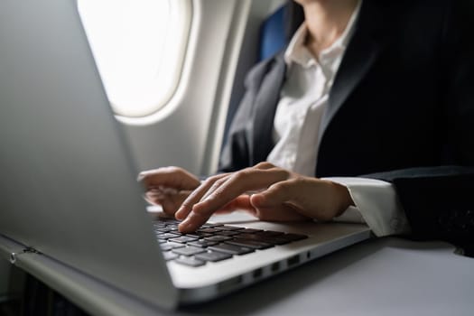 businesswoman flying and working in an airplane in first class, sitting inside an airplane using laptop.