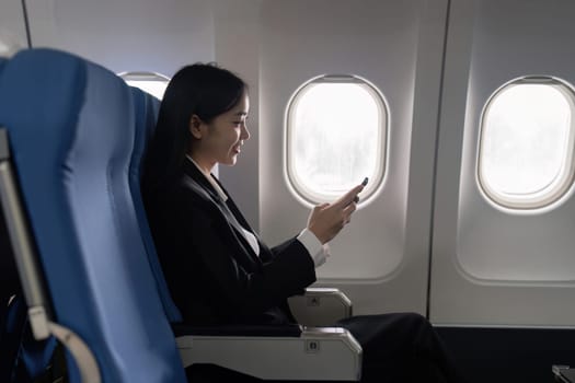 businesswoman flying and working in an airplane in first class, sitting inside an airplane using mobile.