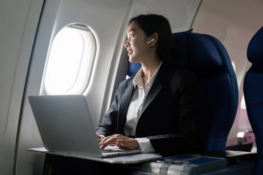 businesswoman flying and working in an airplane in first class, sitting inside an airplane using laptop.