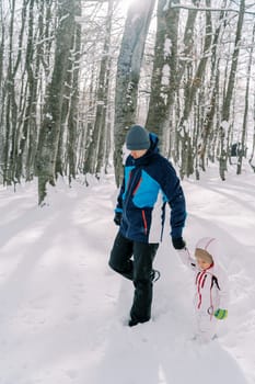 Dad and little girl walk holding hands through a snowy forest, looking down at their feet. High quality photo