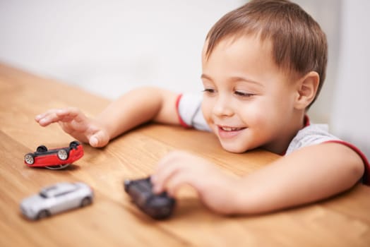 Cars, toys and boy kid by table playing for learning, development and fun at modern home. Cute, sweet and young child enjoying a game with plastic vehicles by wood for childhood hobby at house
