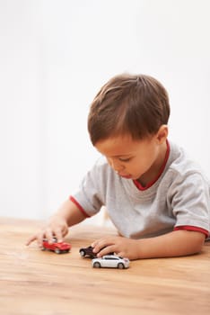 Cars, toys and boy child by table playing for learning, development and fun at modern home. Cute, sweet and young kid enjoying a game with plastic vehicles by wood for childhood hobby at house