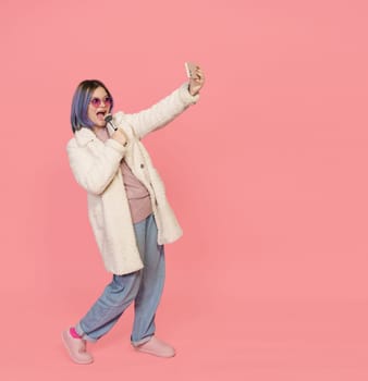 Girl Enjoys Karaoke With Make-Up Brush As Microphone In Selfie Camera Of Mobile Phone. The Image Radiates Positivity And Joy, Showcasing Vibrant And Expressive Mood. Cheerful Karaoke Session With Her Mobile Phone. . High quality photo