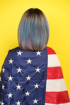 Patriotic Pride And Freedom Spirit Of United States And Its Cultural Richness. Girl With Multicolored Hair Covered With American Flag, Isolated On Yellow Backdrop, Backside View. High quality photo