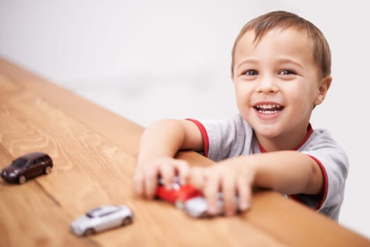 Cars, toys and boy kid by table playing for learning, development and fun at modern home. Cute, sweet and portrait of child enjoying a game with plastic vehicles by wood for childhood hobby at house
