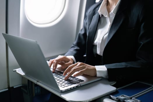 businesswoman flying and working in an airplane in first class, sitting inside an airplane using laptop.