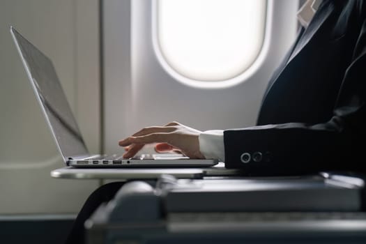 businesswoman flying and working in an airplane in first class, sitting inside an airplane using laptop.