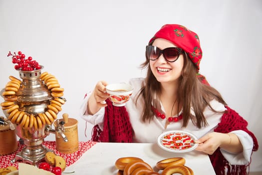 A fashionable modern girl in stylized folk clothes at table with a samovar, bagels and tea for the Orthodox holiday of Maslenitsa and Easter. Funny photo shoot for a young woman