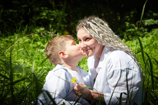 Funny mother with dreadlocks and fat boy happy hugging and kissing in the woods on a sunny summer day