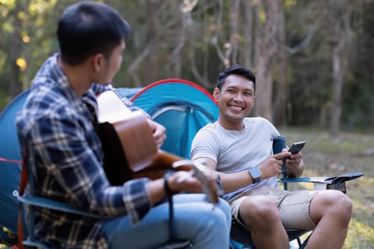 Asian LGBTQ couple enjoying nature, camping with tents in the forest area by the river, playing guitar..