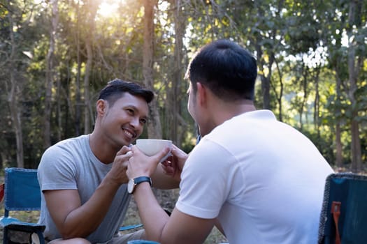 Asian LGBTQ couple drinking coffee in a romantic camping tent. LGBTQ couple drinking coffee in a camping tent, enjoying nature, forest, camping atmosphere, LGBTQ, gay, gay men..