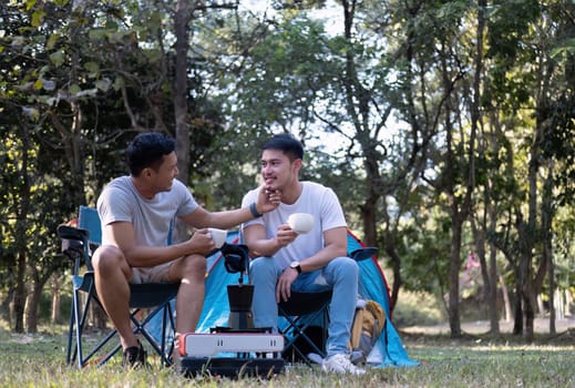 Asian LGBTQ couple drinking coffee in a romantic camping tent. LGBTQ couple drinking coffee in a camping tent, enjoying nature, forest, camping atmosphere, LGBTQ, gay, gay men..