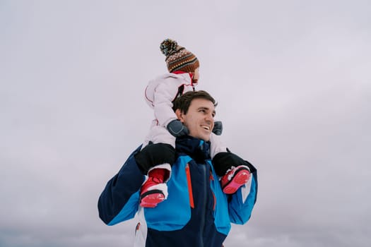 Dad with a little girl on his shoulders stands against the background of a cloudy sky looking to the side. High quality photo
