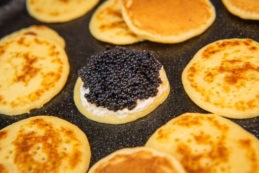 Blinis with black caviar and cream cheese, on a festive dish, mini pancakes, an elegant appetizer, High quality photo