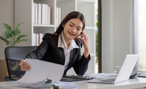 Cheerful Asian businesswoman talking on the phone working in modern office Happy Asian businesswoman company manager wearing a suit is talking on the phone