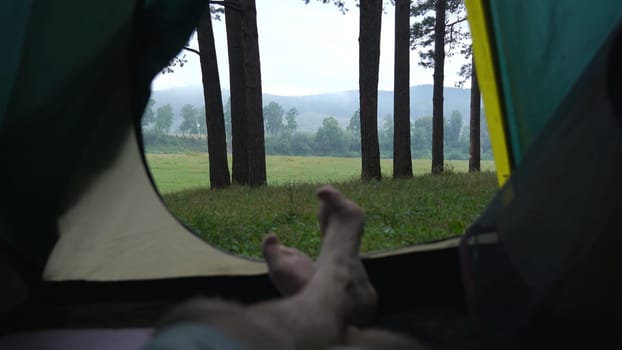 Legs of a man resting in a tent against the background of the forest