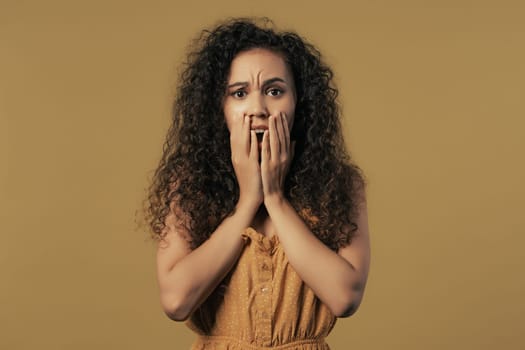 Woman afraid of something, she in shock on yellow backdrop.Holding head, screaming. High quality photo