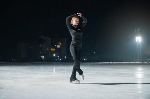 Beautiful young woman ice skating and performing short program over city outdoor ice arena. Winter activities concept