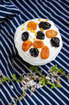 Easter cake, decorated with dried apricots and prunes, stands on a striped blue apron, a flowering branch. Easter religious holiday concept