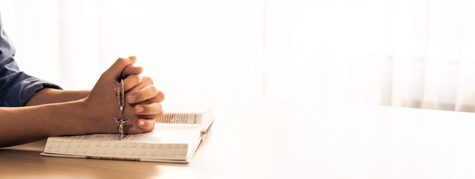 Asian male folded hand prayed on holy bible book while holding up a pendant crucifix. Spiritual, religion, faith, worship, christian and blessing of god concept. Blurring background. Burgeoning.